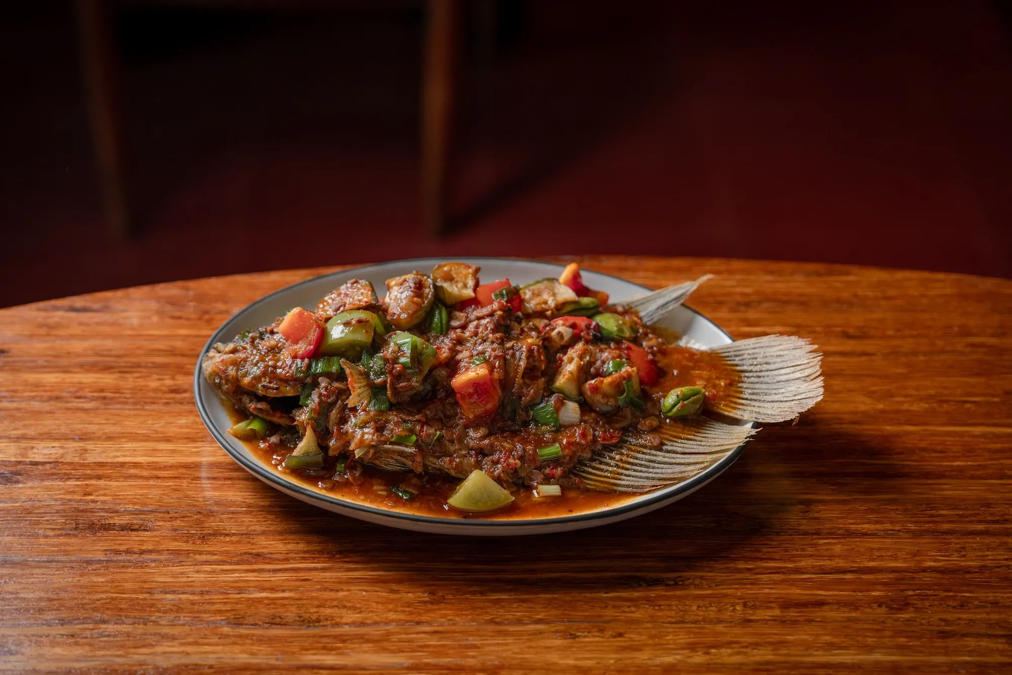A whole fish under a chunky tomato and chilli sauce, on an oval plate