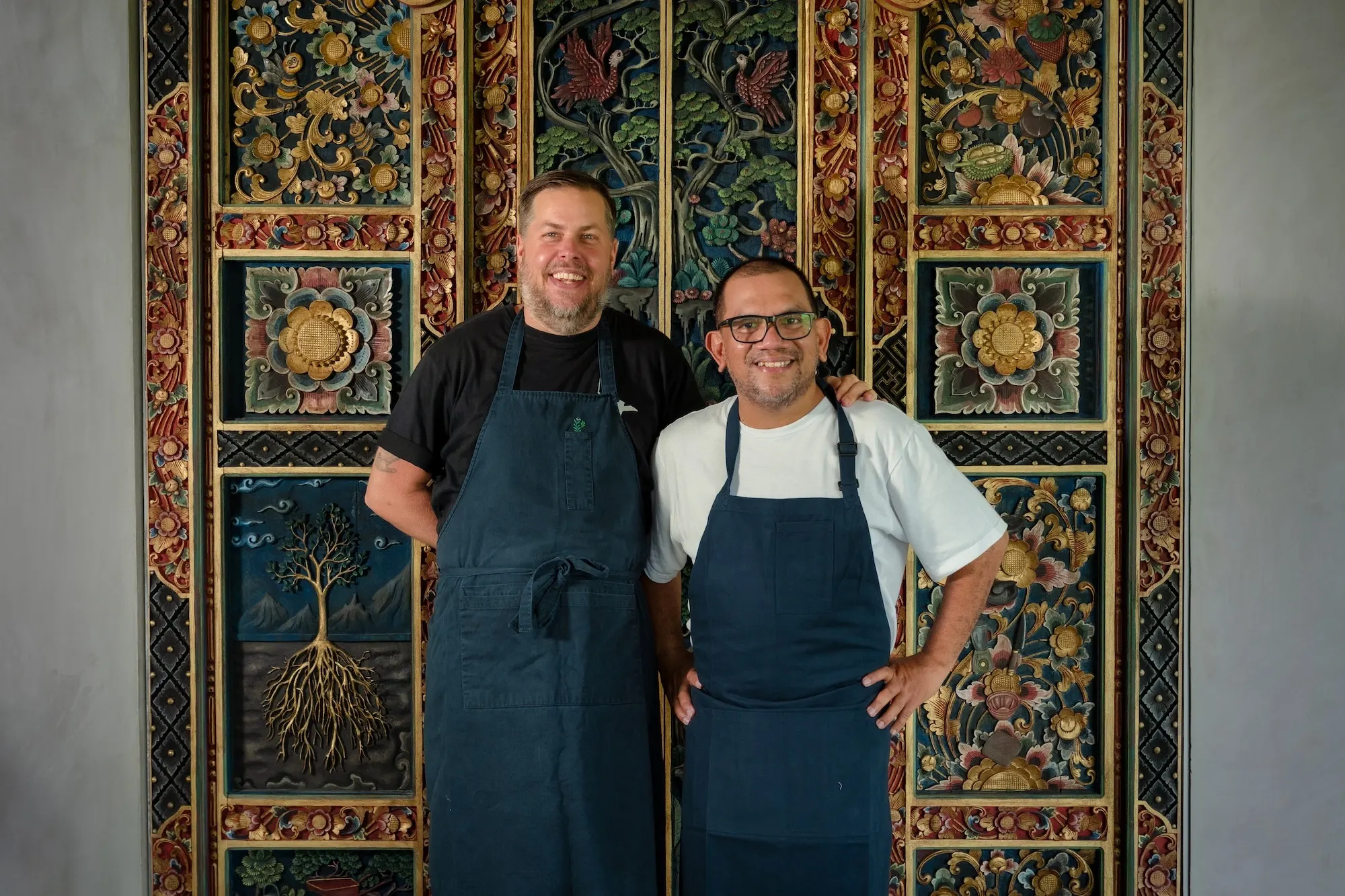 Founders Eelke Plasmeijer and Ray Adriansyah in their aprons, in front of a carved Balinese door