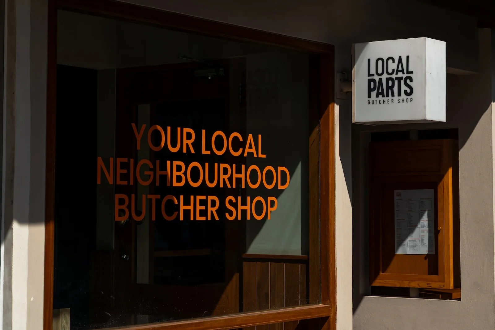 The Local Parts shopfront — a lit butcher shop sign beside a window lettered "Your local neighbourhood butcher shop"