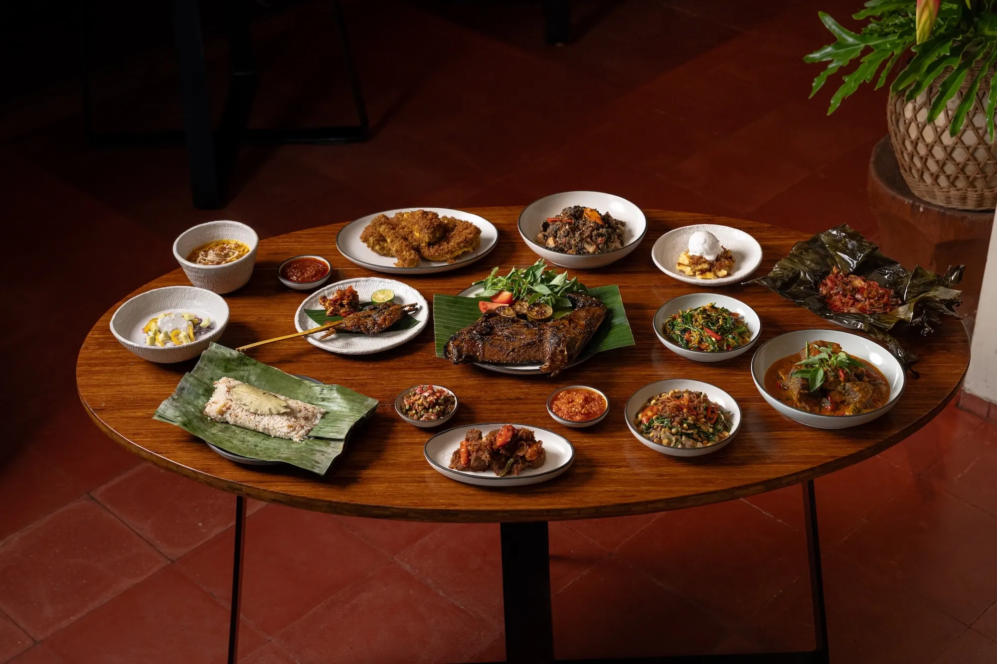 A table laid with the full spread — bowls of dishes, sambals and banana-leaf parcels