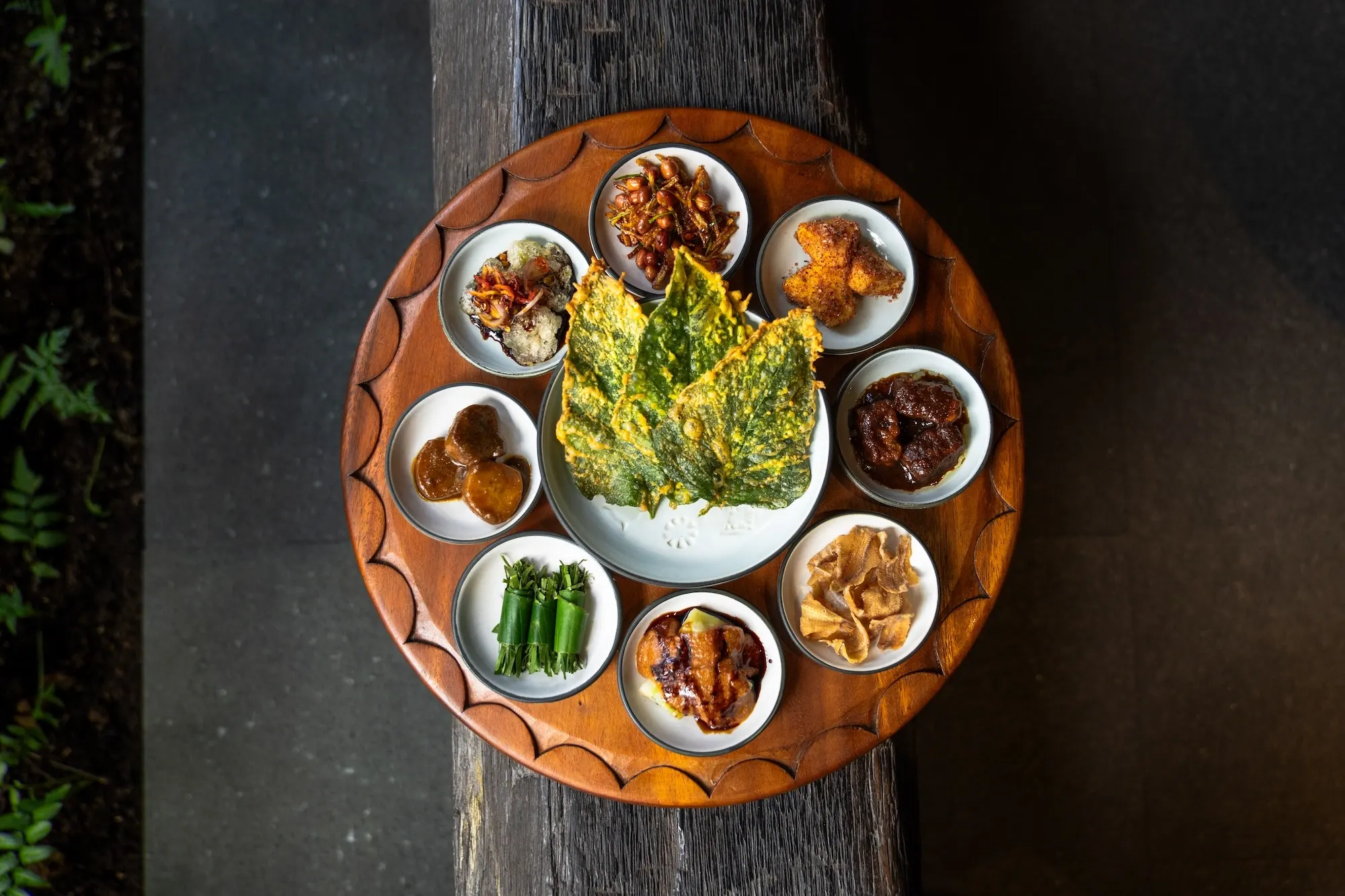 A rijsttafel platter — small bowls of dishes and sambals ringing a herb omelette, on weathered wood