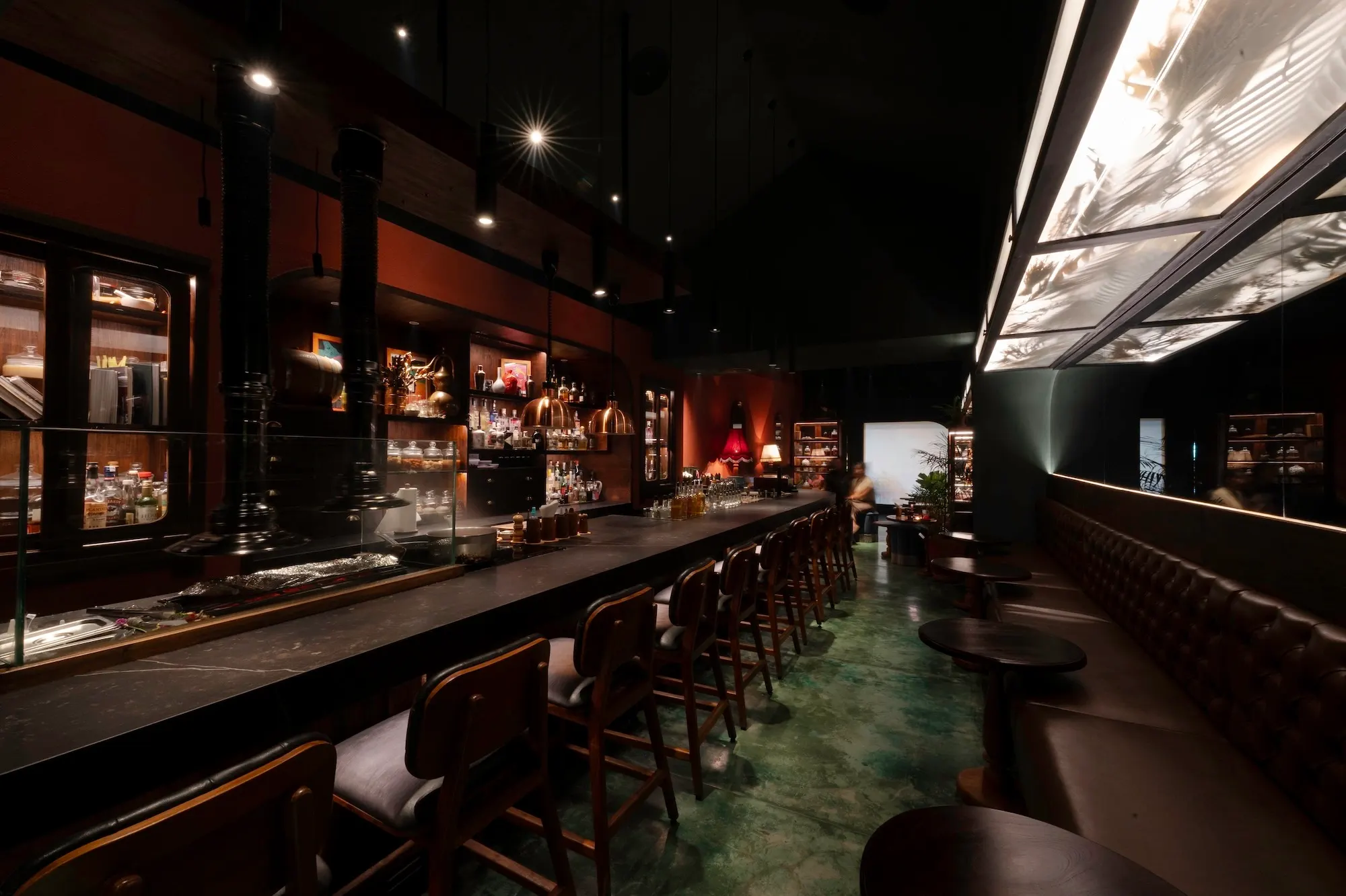 The long bar at Night Rooster — a row of stools under low light, bottles glowing on the back bar