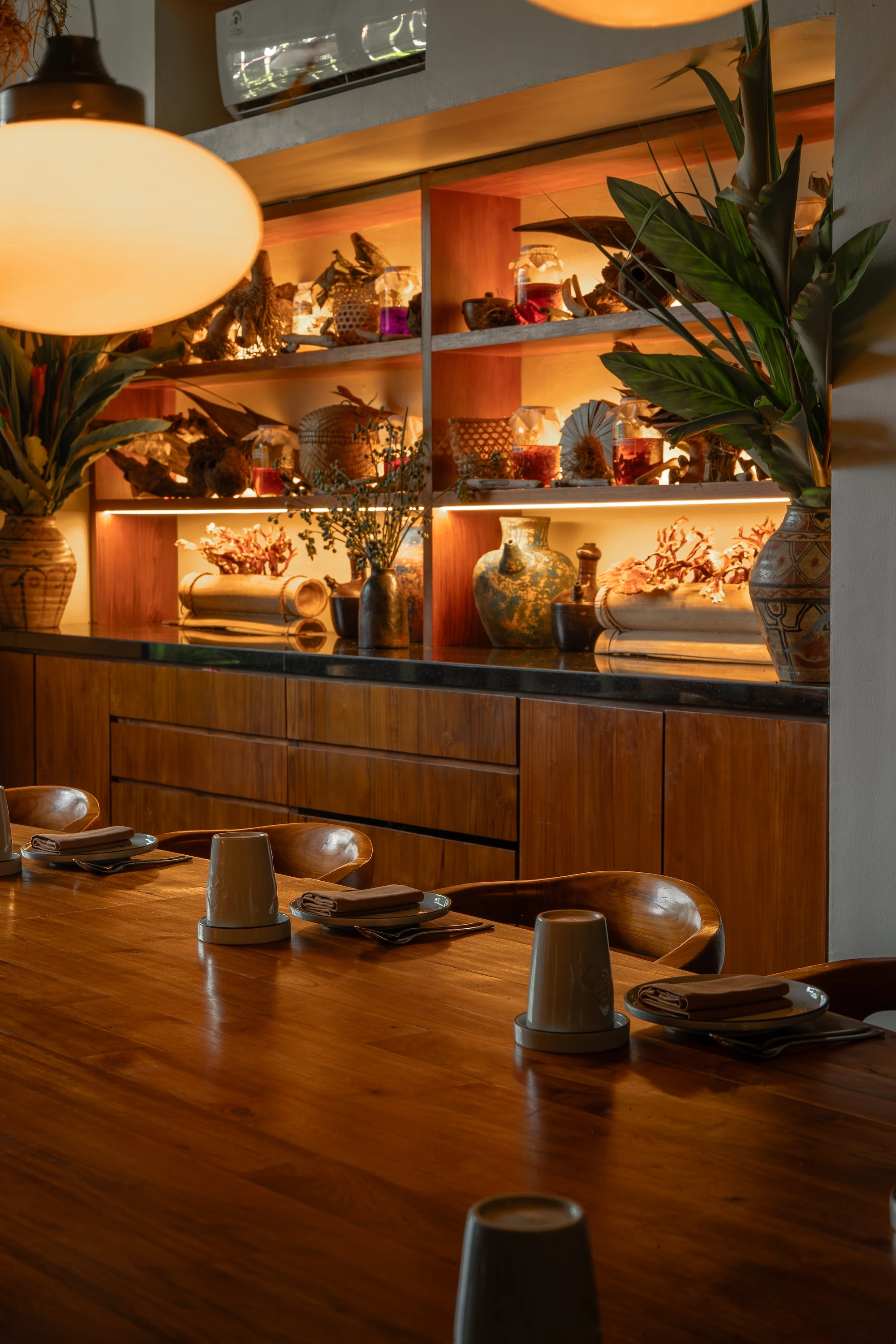 The end of the private dining table, with lit shelves of ceramics, jars and dried coral behind it