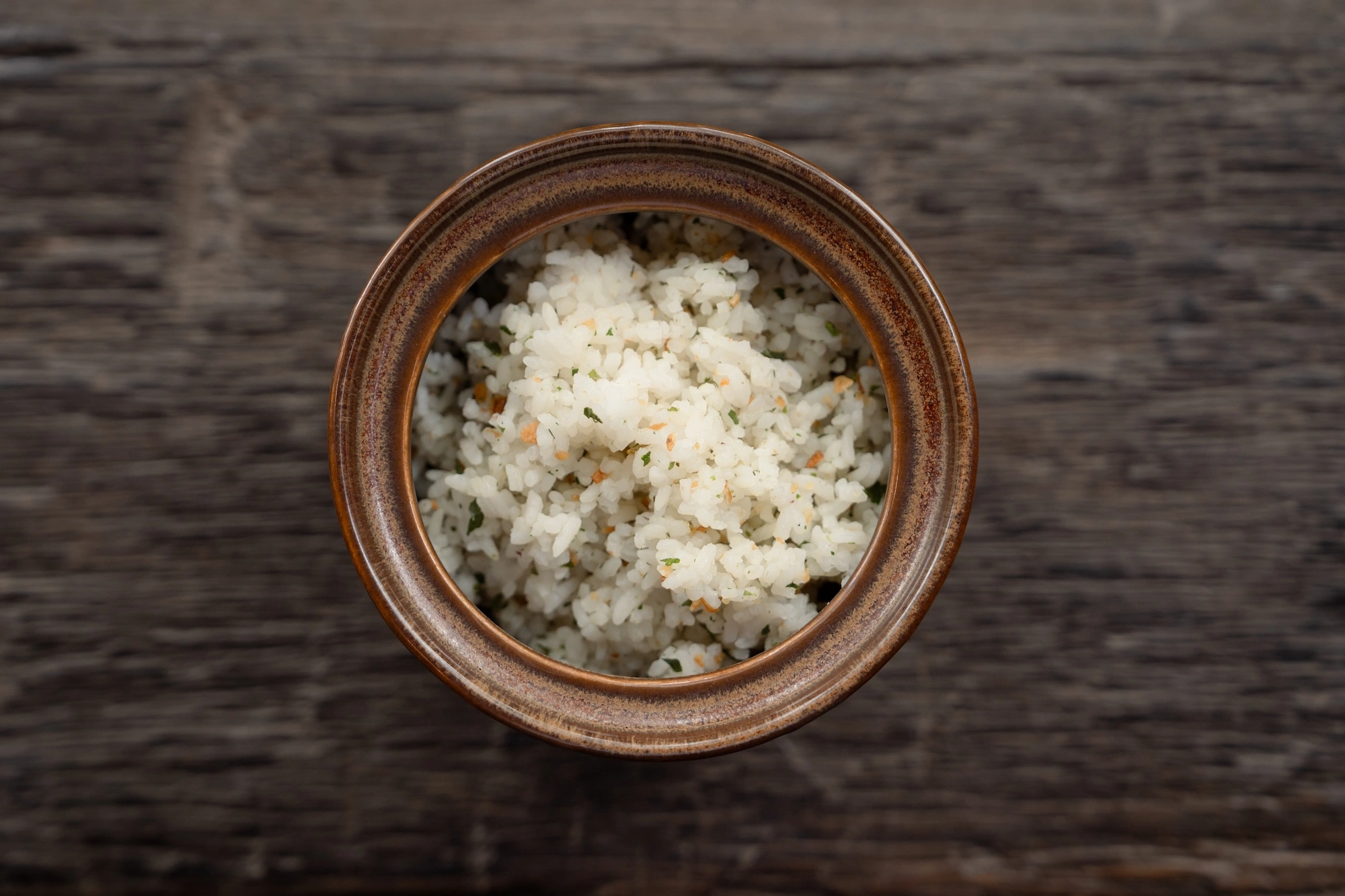 A clay pot of herbed rice on weathered wood, seen from above